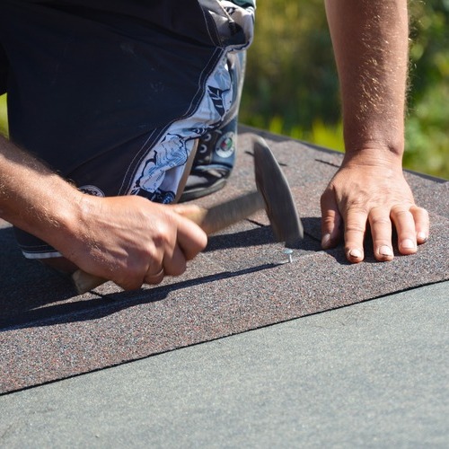 roofer nailing down asphalt shingle roofing